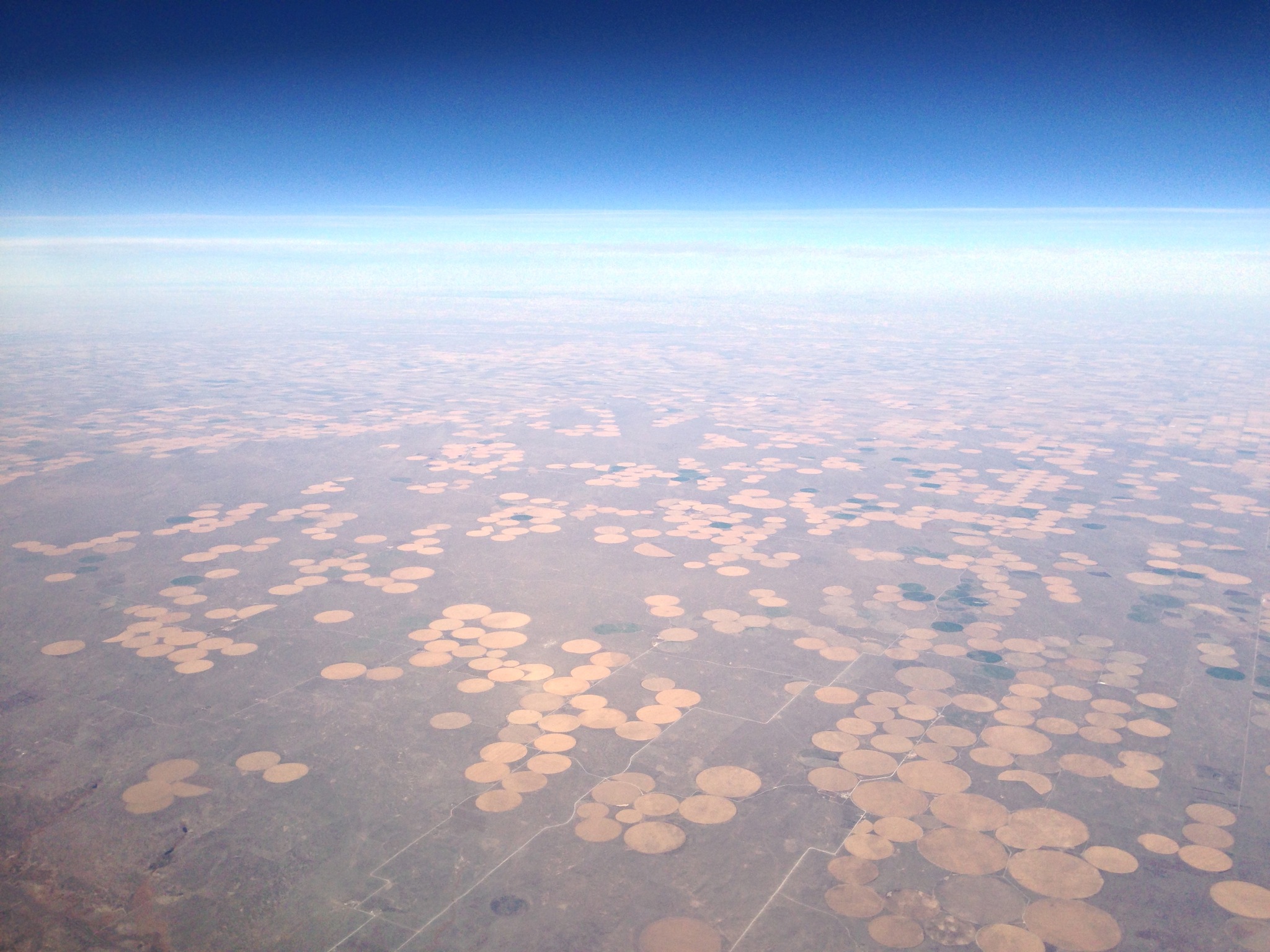 overlooking clusters of circular fields, from high above, toward a distant, blue horizon